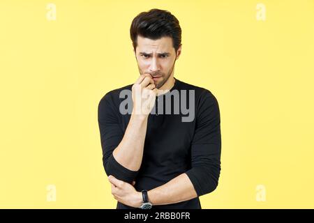 Serious houghtful man have a doubt over yellow background. Uncertain, thinking, pensive concept Stock Photo