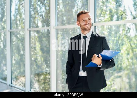 Handsome smiling businessman with clipboard in a bright modern office with copy space. business concept Stock Photo