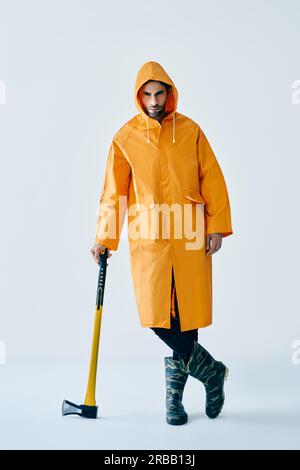 Full length portrait of young handsome man in bright raincoat holding big axe. Brutal male, lumberjack, fisherman with ax Stock Photo