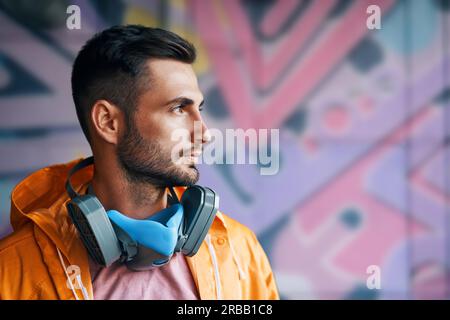Portrait of handsome street artist staying on his graffiti painting background with copy space. Urban art concept Stock Photo