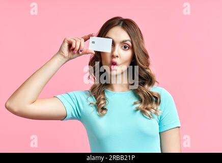 Portrait of a funny young woman having fun, making fish kisses face holding credit closing eyes isolated over pink background. foolish grimaces Stock Photo