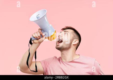 Funny young man shouting loud holding a megaphone over pink background. Announcement, communication concept Stock Photo