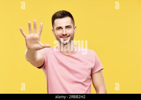 Portrait of smiling man with hand raised in greeting over yellow background. High five, hello concept Stock Photo
