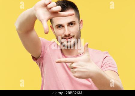 Portrait of smiling handsome man making frame with fingers and looking at camera on yellow background Stock Photo