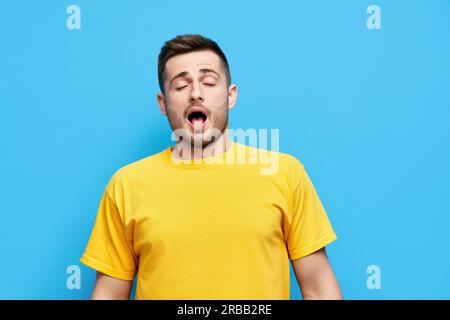 Yawning or sneezing young man over blue studio background with open mouth Stock Photo