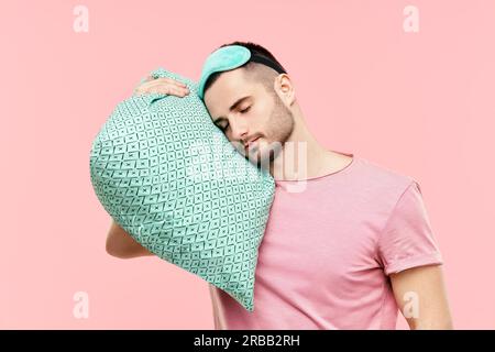 Young handsome man sleeping holding pillow in hands over pink background. Relax, tired concept Stock Photo