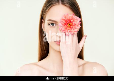 Close up portrait of beautiful young woman covering her eye with flower. Female beauty, spa, clean skin concept Stock Photo
