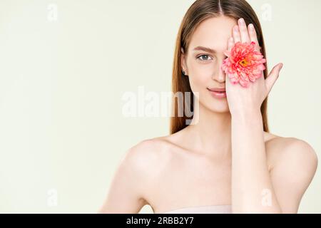 Close up portrait of beautiful young woman covering her eye with flower. Female beauty, spa, clean skin concept. Copy space Stock Photo
