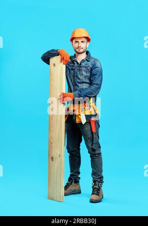 Full length portrait of young handsome carpenter hold pile of lumber woods over blue background looking to camera Stock Photo