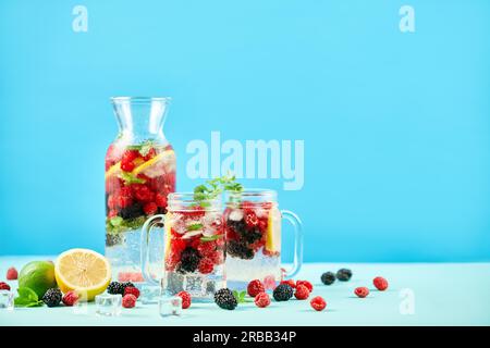 Fresh berries cocktails in glass jars and jug with copy space. Fresh summer cocktail with mix of berries, lemon and mint on blue background. Party Stock Photo