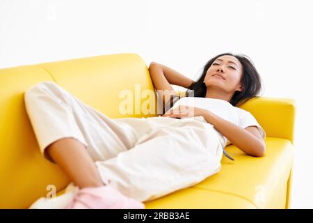Young pretty woman closed her eyes lying on yellow sofa and relaxing after busy day. Rest, comfort concept Stock Photo