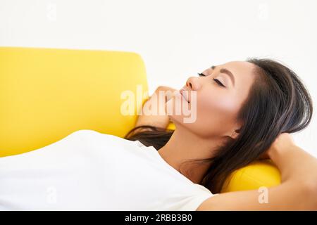 Young pretty woman closed her eyes lying on yellow sofa and relaxing after busy day. Rest, comfort concept Stock Photo