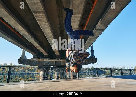 Young man break dancer doing somersault acrobatic stunts dancing on urban background. Street artist breakdancing outdoors Stock Photo