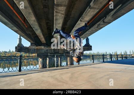 Young man break dancer doing somersault acrobatic stunts dancing on urban background. Street artist breakdancing outdoors Stock Photo