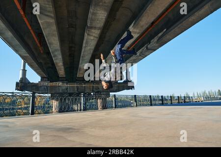 Young man break dancer doing somersault acrobatic stunts dancing on urban background. Street artist breakdancing outdoors Stock Photo