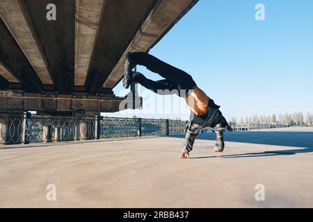 Young man break dancer doing somersault acrobatic stunts dancing on urban background. Street artist breakdancing outdoors Stock Photo