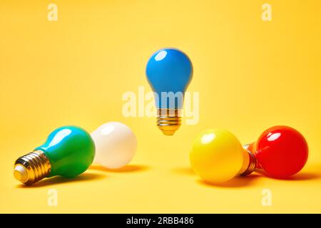 Creative layout with multicolored lightbulbs on yellow background. Blue light bulb levitate in air. Idea symbol, business creativity, inspiration Stock Photo