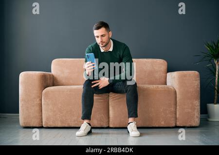 Relaxed man sitting on couch using hsi mobile phone. Social media concept Stock Photo