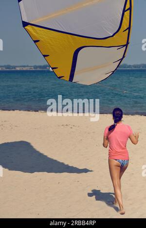 Young woman at the seaside with large colorful kite or kite surfing sail standing on a sandy summer beach in her swimming costume Stock Photo