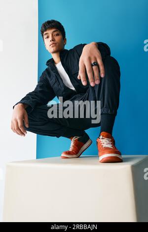 Confident young trendy Mixed-race man posing in studio sitting on big cube. Youth culture, millennials concept Stock Photo