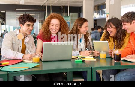 Group smiling young Caucasian college students preparing for classes gathered in campus cafeteria.  Stock Photo