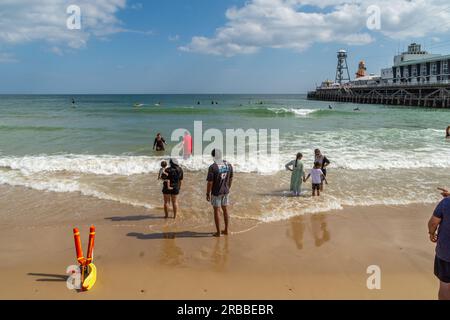 Bournemouth, UK - July 1st 2023: People standing on the beach with their feet in the sea in front of Bournemouth Pier. Stock Photo