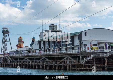 Bournemouth, UK - July 1st 2023: People passing the pier on the zip line on the pier to beach zip wire. Stock Photo