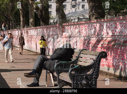 An elderly man sitting on a park bench next to the The National Covid Memorial Wall, London, England, UK. Stock Photo