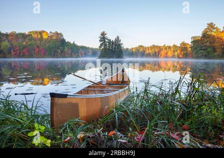 Yellow canoe on shore of calm lake with island and trees in fall color in northern Minnesota Stock Photo