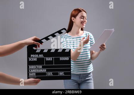Actress performing role while second assistant camera holding clapperboard on grey background, selective focus Stock Photo