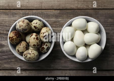 Unpeeled and peeled boiled quail eggs in bowls on wooden table, flat lay Stock Photo