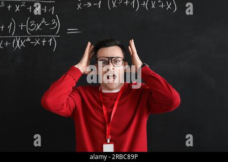 Stressed Math teacher near blackboard in classroom Stock Photo