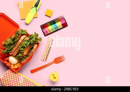 Stationery and lunchbox with tasty food on pink background Stock Photo