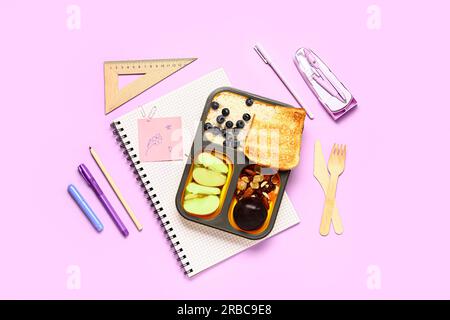 Different stationery and lunchbox with tasty food on lilac background Stock Photo