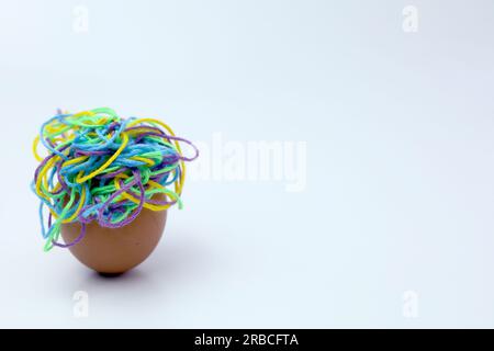 Close-up view cracked eggshell on white background with colorful tangled threads inside and with copy space for insert text or wording Stock Photo