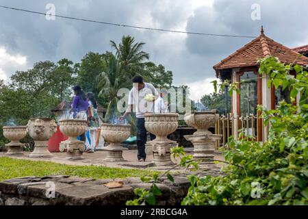 Visitors to the Buddhist Sacred Temple of the Tooth Relic at Kandy in Sri Lanka light incense sticks in pots. Stock Photo