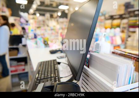 Selective focus. Partial view of currency counter, note counting machine and black blank PC monitor on the reception desk, in a school stationery stor Stock Photo