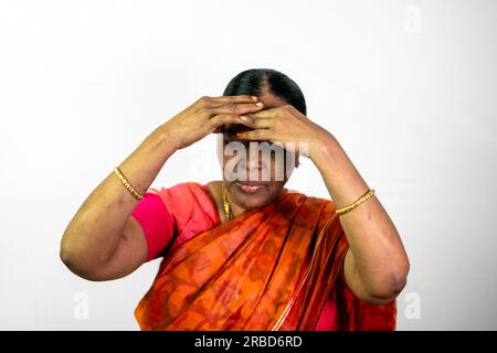A close-up portrait of a South Indian woman making a headache gesture with her hand. She is standing against a white background and is wearing a tradi Stock Photo
