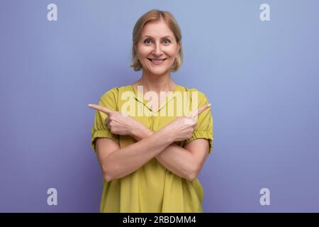 cute blond middle aged woman with an idea points her finger to the side in studio Stock Photo