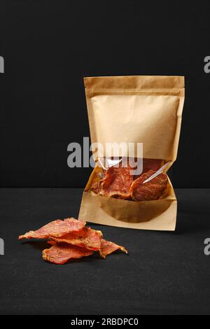 Jerky pork meat in paper pack on black background Stock Photo