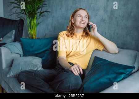 Happy cheerful young woman talking on the phone at home, smiling teen girl making answering call by cellphone sitting on chair, beautiful lady having Stock Photo