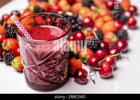 A glass of red berry detox juice with a straw, ripe red berries on a plain light blue table Stock Photo