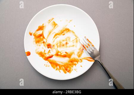 Dirty white ceramic plate with tomato sauce stains, food leftovers and fork, top view Stock Photo