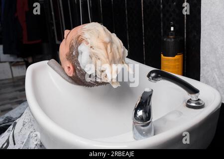 Soapy head of a guy's client in shampoo over the sink washing his hair before a haircut in a barbershop. Stock Photo