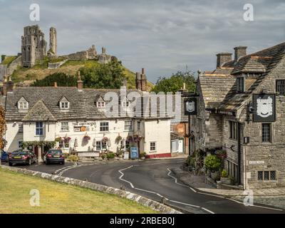The imposing Corfe Castle rises above The Greyhound and Bankes Arms Hotel in the centre of the famous Dorset village. Stock Photo