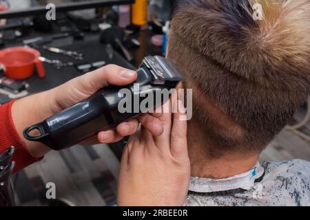 The hands of a professional barber man with a clipper cut the hair near the ear of a client, a hairdresser's guy. Stock Photo