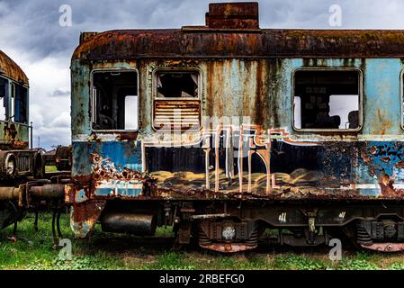 Old rusty electric multiple unit train decommissioned and abandoned on railway siding on green grassy field Stock Photo