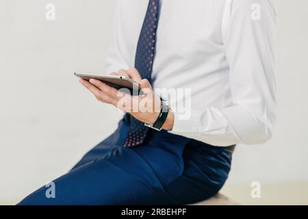 Successful businessman in white shirt, black trousers, tie holds tablet, checks notification. Isolated on white background. Stock Photo