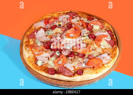 Pizza with bacon cheese and herbs on a wooden plate with cheese and cherry tomatoes. On a colored background. copy space Stock Photo