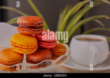Selection of macaroons stacked up on a glass cake stand with a beverage in the background. Stock Photo